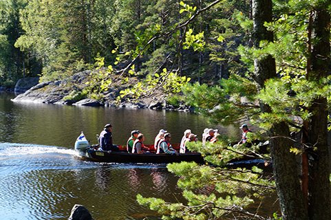Aurinkoisena päivänä veneessä istuu henkilöitä retkellä Repovedellä , ympärillä kalliota ja vihreää metsää